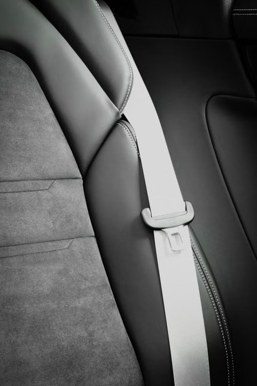 Light coloured seat belt webbing with its latch plate running down a dark vehicle seat